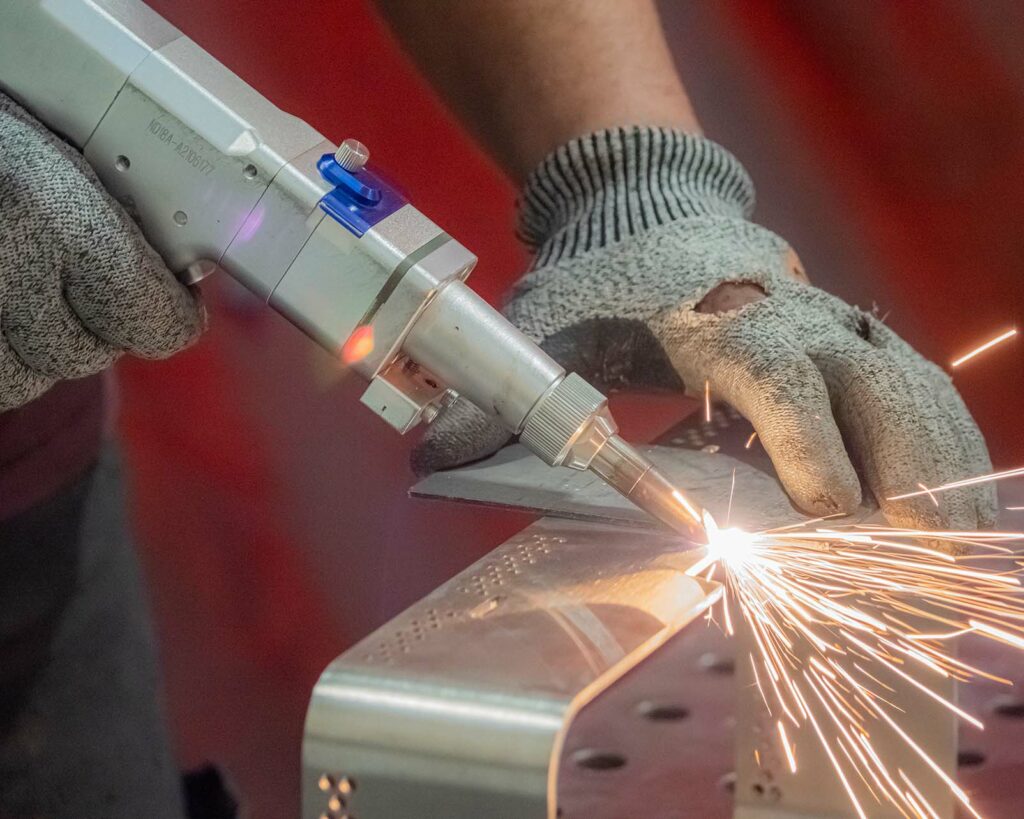 First picture of a technician welding a metal piece with laser, with visible foils and protective gloves, to the R&G Metal Shaping installations.